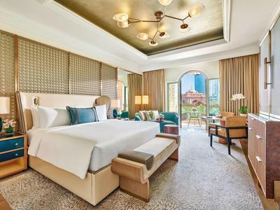 Helles Hotelzimmer mit großem Bett, Sitzbereich und Balkon mit Blick auf die Stadt.