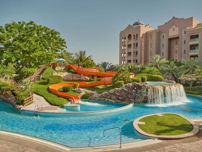 Hotelpool mit Wasserrutschen, Wasserfall und umgebender Vegetation bei sonnigem Himmel
