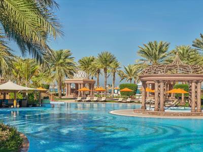 Velký resortní bazén s palmami, slunečníky a zastřešeným barem u bazénu za jasné oblohy.