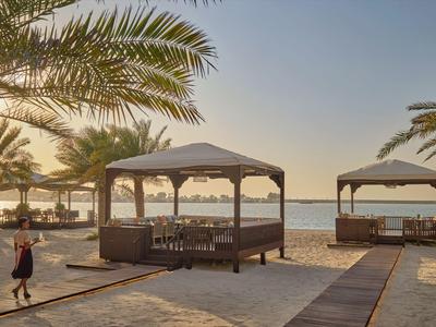 Strand mit Palmendächern und Sitzbereichen bei Sonnenuntergang neben dem Meer.