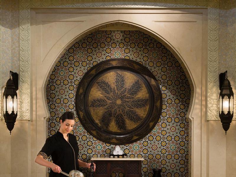 Ein Mann gießt Tee in einem eleganten, orientalisch inspirierten Raum mit geschwungenen Wänden.