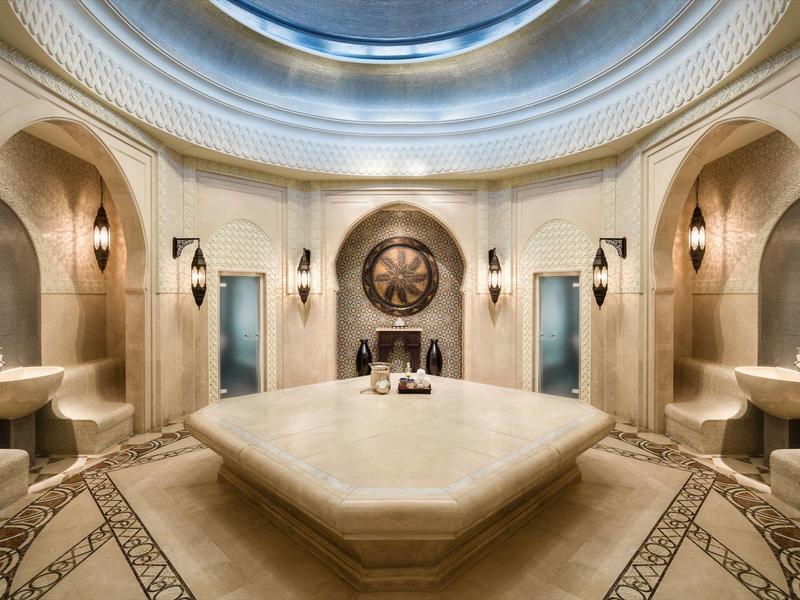 Luxuriöses Hammam mit Marmorflecken, Rundbecken und kunstvollen Wandlampen in warmem Licht.