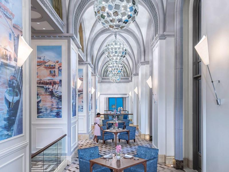 Eleganter Hotelkorridor mit blau gepolsterten Stühlen und großen Wandbildern.