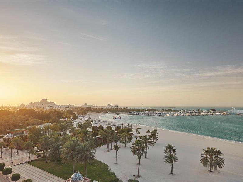 Sonnenaufgang über einem ruhigen Strand mit Palmen und einem Hotel im Hintergrund.