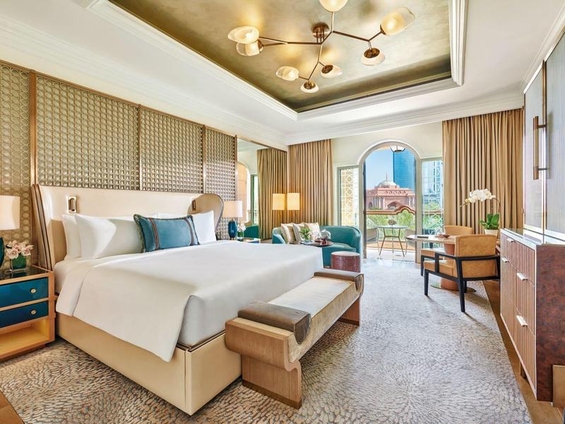 Helles Hotelzimmer mit großem Bett, Sitzbereich und Balkon mit Blick auf die Stadt.