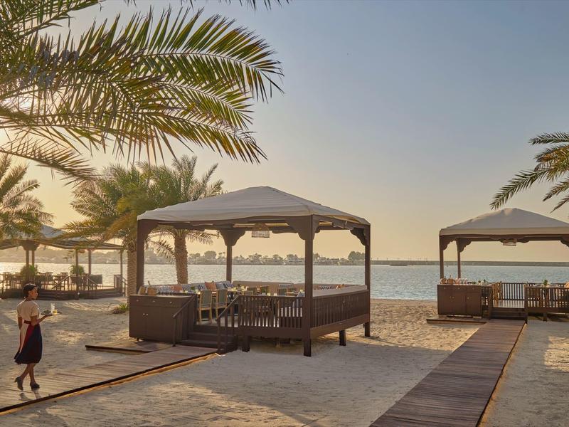 Strand mit Holzpavillons, Palmen und Meer bei Sonnenuntergang