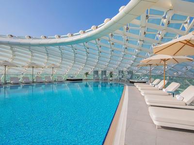 Moderner Poolbereich mit Liegestühlen und Sonnenschirmen unter einer gewölbten Glasüberdachung.