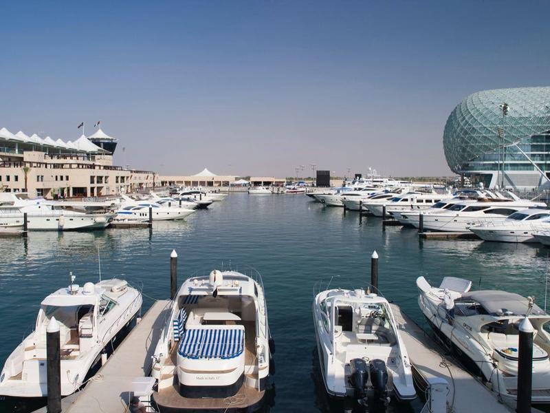 Yachthafen mit weißen Booten, blauem Wasser und moderner Architektur im Hintergrund bei klarem Himmel.