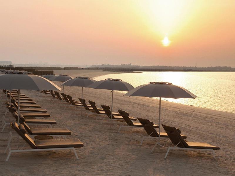 Leere Strandliegen und Schirme am ruhigen Seeufer bei Sonnenuntergang.