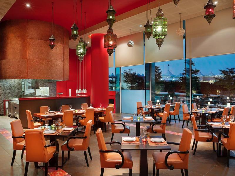 Moderner Restaurantraum mit orangen Stühlen, Holz- und Glas-Tischen, roten Wänden und Hängelampen.