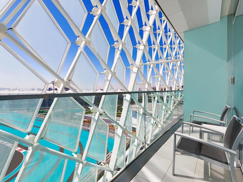 Moderner Balkon mit Metallstühlen, Glasgeländer und großem Fenster mit Gitterstruktur, Blick aufs Meer.