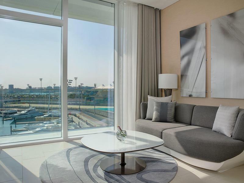 Helles Wohnzimmer mit grauer Eckcouch, runden Teppich, Tisch und großer Glasfront mit Aussicht.