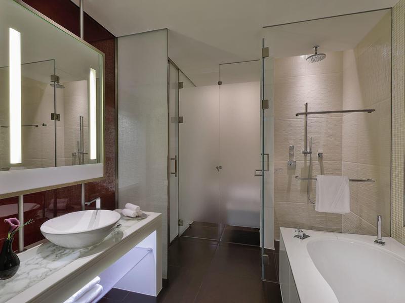 Modernes Badezimmer mit beleuchtetem Spiegel, Waschbecken, Glasdusche und Badewanne.