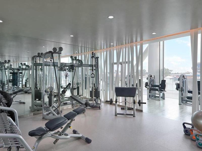 Moderner Fitnessraum mit Geräten, hellen Wänden, großen Fenstern und Blick auf die Stadt.