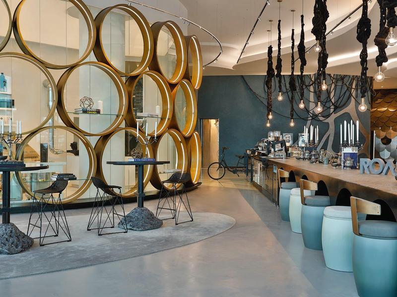 Modern eingerichteter Gastraum mit runden Holzregalen, blauen Hockern und dekorativem Licht.