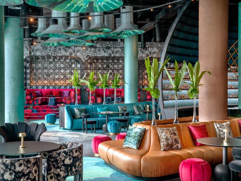 Moderne Lounge mit bunten Sofas, farbenfrohen Kissen und Pflanzen in großem, offnem Raum.