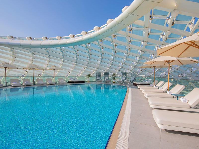 Moderner Außenpool mit glattem blauem Wasser, weißen Liegestühlen und großen Sonnenschirmen.