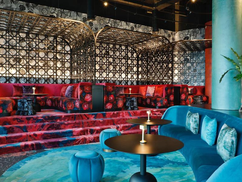 Moderner Lounge-Bereich mit roten Samt-Sesseln, blauen Sofas und geometrischem Wandmuster.