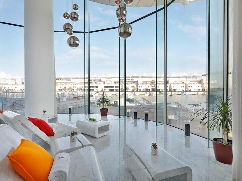 Moderner Wohnraum mit großen Panoramafenstern, weißen Möbeln und bunten Kissen, helle Atmosphäre.