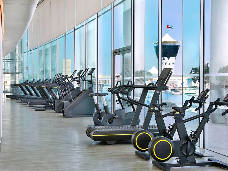 Moderner Fitnessraum mit Cardio-Geräten und Panoramafenstern mit Blick auf den Hafen.