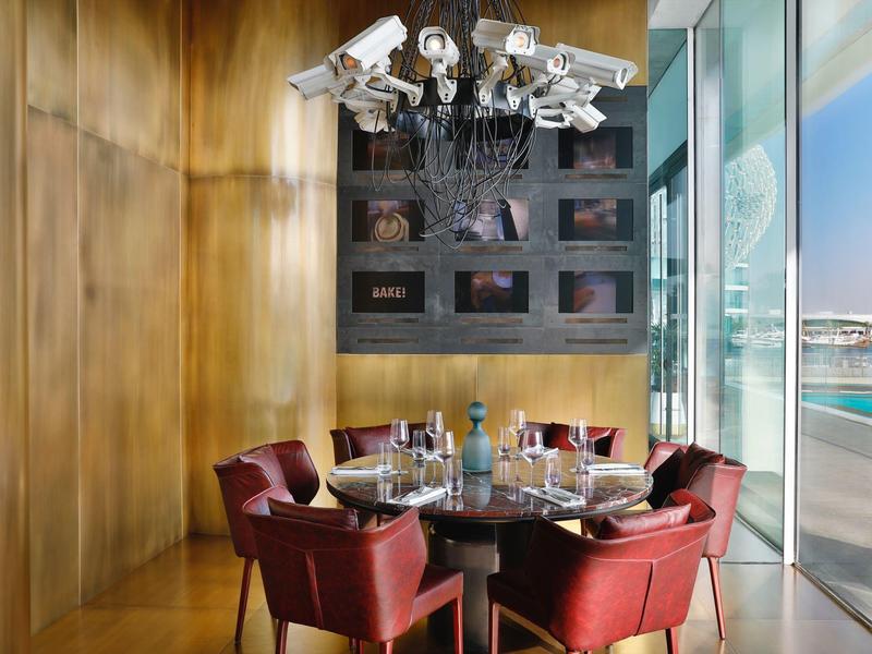 Moderner Essbereich mit rundem Tisch, sechs roten Stühlen, Glasflaschen und sechs Kameras als Deckenlampe.