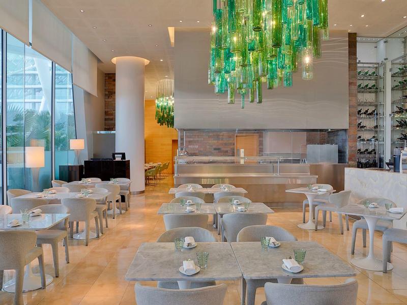 Modernes Restaurant mit grauen Stühlen, runden Tischen und grünem Glasdeckenleuchter.