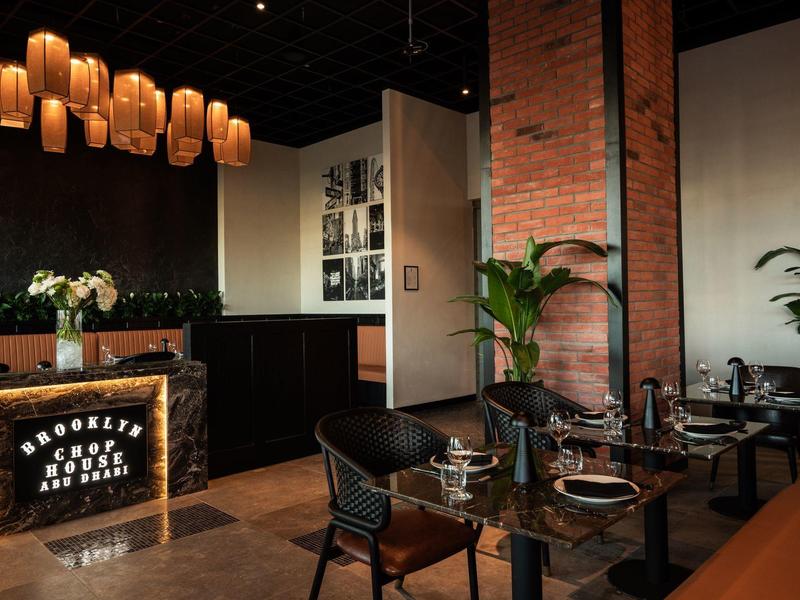 Modern eingerichtetes Restaurant mit Holz- und Backsteinelementen, warmem Licht und elegant gedeckten Tischen.