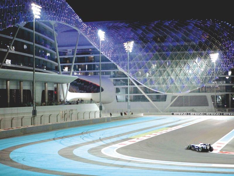 Moderne Rennstrecke bei Nacht mit beleuchteter Glasstruktur und Rennwagen auf der Piste.