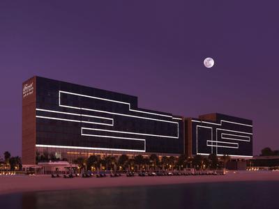 Modernes Hotel mit markanten Linien bei Nacht am Wasser mit Mond im Hintergrund.