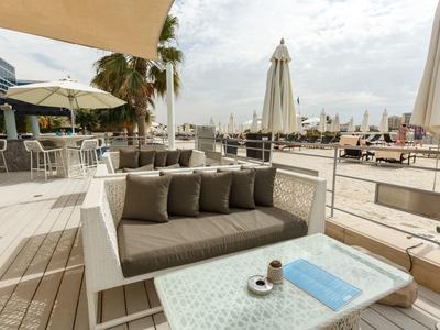 Moderne Außenterrasse mit beigem Sofa, Kissen, Tischen, Sonnenschirmen und städtischer Skyline im Hintergrund.