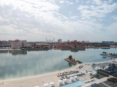 Blick auf eine ruhige Lagune mit Strand, Häusern am Ufer und wolkigem Himmel.