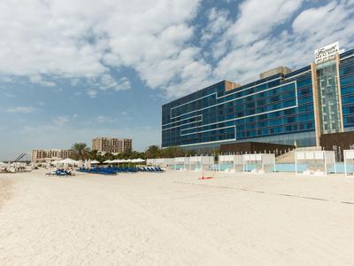 Breiter Sandstrand mit Liegestühlen und modernen Hotels im Hintergrund unter bewölktem Himmel.