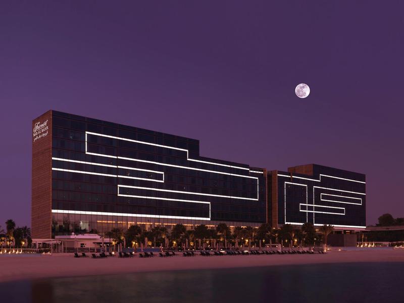 Zwei moderne, beleuchtete Gebäude am Wasser bei Nacht mit einem hellen Vollmond im violetten Himmel.