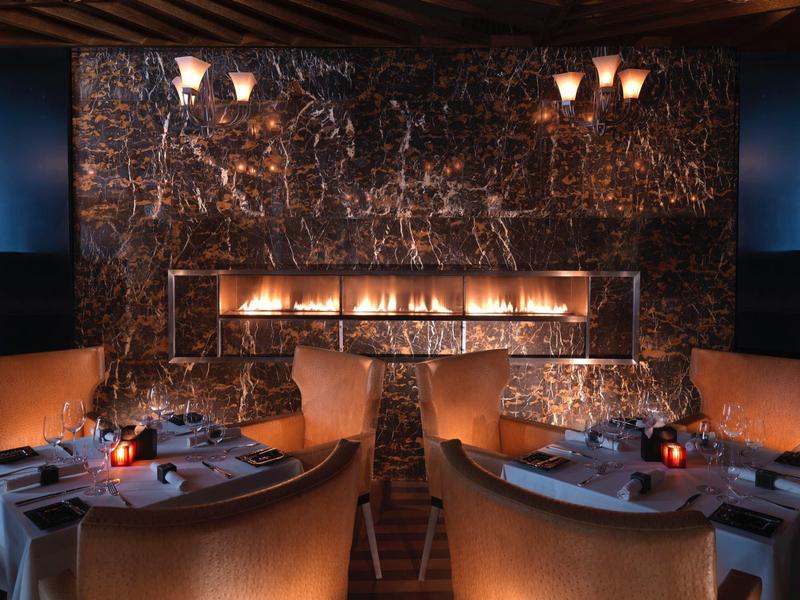 Elegantes Restaurant mit Kamin, dunklen Marmorwänden und warmen, gedämpften Lichtern.