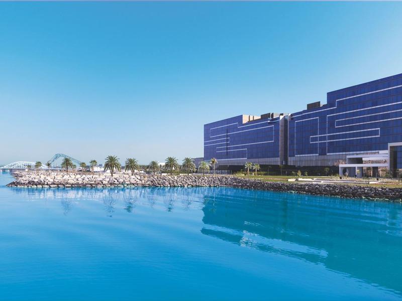 Großes modernes Gebäude am Ufer mit klarem blauem Wasser und blauem Himmel im Hintergrund.