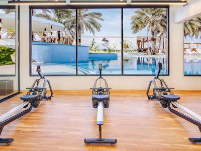 Innenansicht eines Fitnessraums mit Rudergeräten und Ausblick auf einen Pool und Palmen.