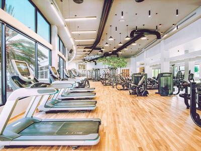 Großer Fitnessraum mit Laufbändern und Kraftgeräten vor großen Fenstern und Holzboden