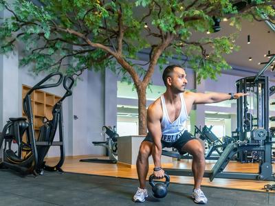 Mann trainiert mit Kettlebell im Fitnessstudio vor einem Spiegel und Baumdeko.