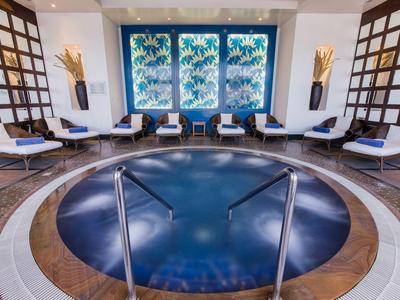 Runder Whirlpool mit Edelstahlgeländern, bequemen weißen Stühlen und großen blauen Fenstern.