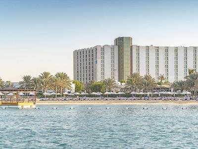 Hotel am Ufer mit Poolbereich, Palmen und ruhigem Wasser im Vordergrund.