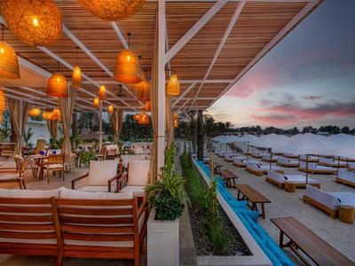 Offene Strandbar mit hölzernen Möbeln und Laternen bei Sonnenuntergang.