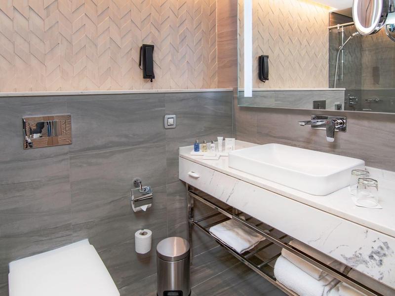 Modernes Badezimmer mit Wand-WC, großem Waschbecken und beleuchtetem Spiegel.