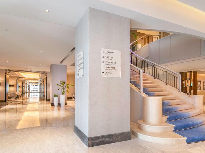 Heller Hotel-Flur mit breiter Treppe, moderner Einrichtung, Pflanzen und warmem Licht.