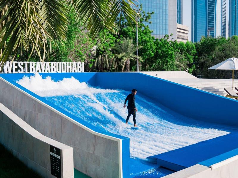 Ein Surfer auf künstlicher Welle vor Palmen und hohen Gebäuden bei West Bay Dubai.