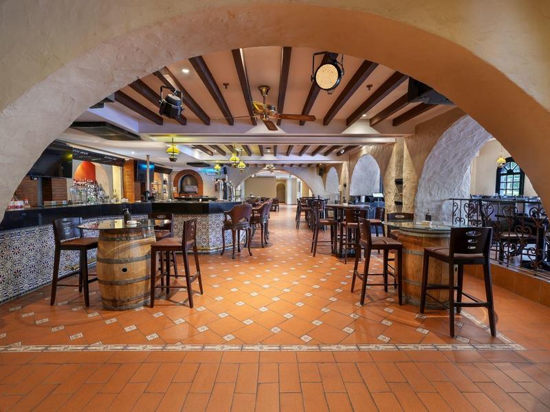 Rustikale Bar mit Holztischen, Stühlen, offenem Kamin und sichtbaren Deckenbalken in warmen Farben.