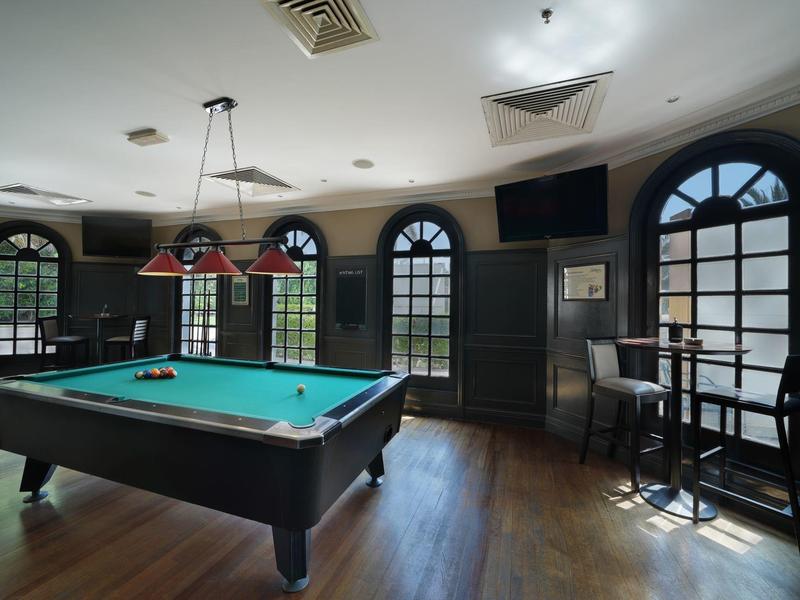 Ein heller Raum mit Billardtisch, drei runden Fenstern und hohen Stühlen an einem kleinen Tisch.