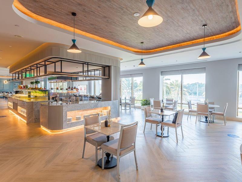 Helles, modernes Café mit großen Fenstern, Holzboden, gemütlichen Tischen und Deckenbeleuchtung.