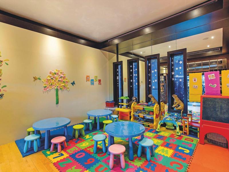 Bunter Spielraum mit kleinen Tischen, Hockern, Puzzle-Teppich und Wanddekorationen.