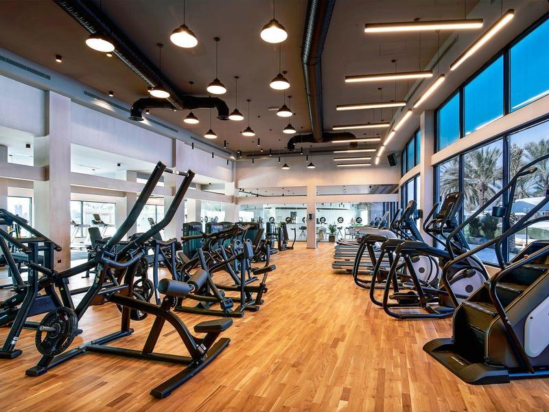 Moderner Fitnessraum mit Holzboden, großen Fenstern und verschiedenen Trainingsgeräten.