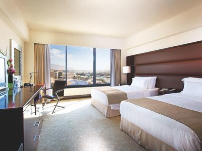 Modernes Hotelzimmer mit zwei Betten und großer Fensterfront mit Stadtblick.